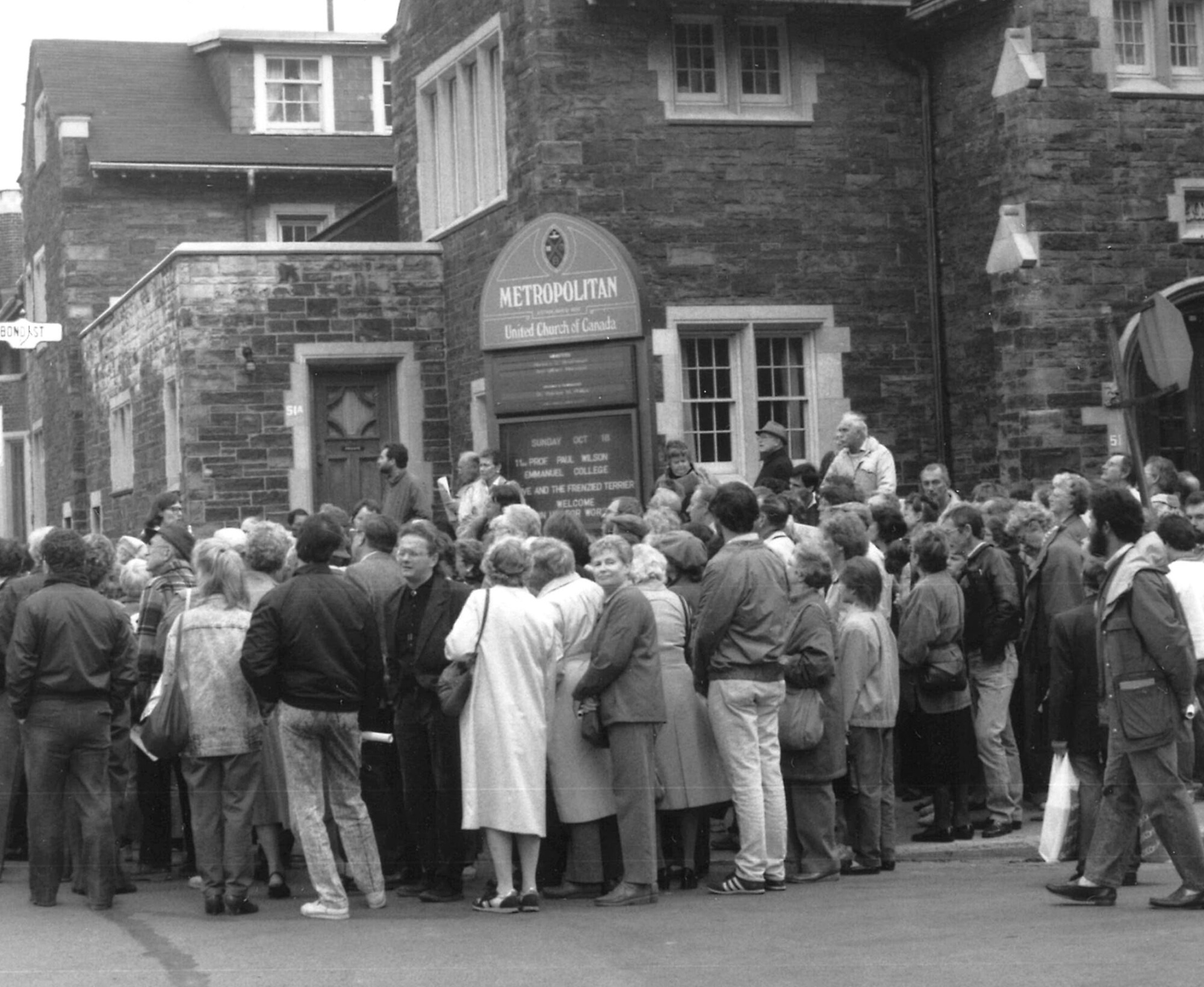 A crowd of approximately 75 people dressed in fall clothing outside the Metropolitan United Church on Bond Street participating in the 